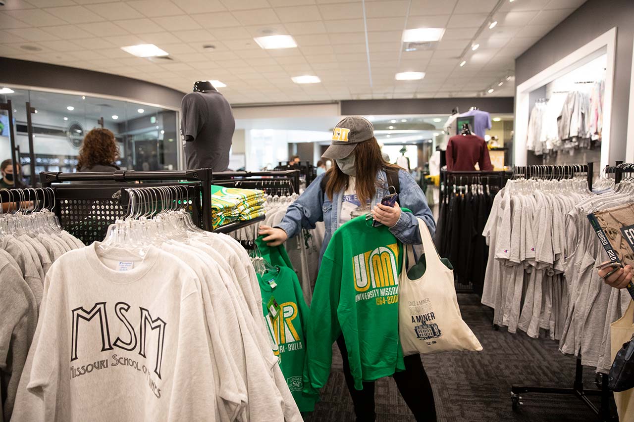 Student shops in store holding UMR sweatshirt and canvas gift bag.